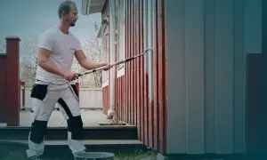 Ett tegelhus med en tillbyggnad i mörk träpanel under ett tegeltak. Uteplats med möbler och grönskande trädgård.