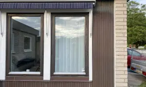 Två fönster med mörkbrun karm och en randig markis ovanför. En ny fasad utanpå den gamla, med träpanel och tegel.