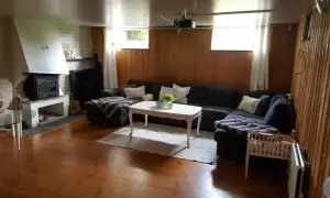 En mysig gillestuga med stor soffa, öppen spis och träpaneler. Perfekt för att renovera gillestuga till ett modernt allrum.
