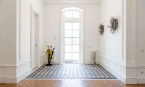 Vacker hall med gammalt hus-känsla. Ett mönstrat golv möter ett fiskbensparkettgolv. Paraplyställ och dörr mot ljuset.