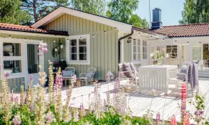 Ett charmigt hus med ljusgröna väggar, perfekt för att måla huset i sommar. Trädäck med vita möbler och blommor.