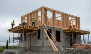 Byggare i reflexvästar arbetar på ett hus under uppbyggnad. Träkonstruktionen reses på en grund av betongblock.