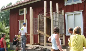 Byggnation av glasveranda entre. Människor hjälps åt att bygga en ny entré med gamla fönster.