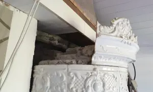 Detalj av en vit, ornamenterad kakelugn i lerbruk. En del av kaklet är skadat och visar den inre konstruktionen.