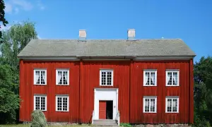 Rött trähus med vita fönster och skorstenar. En höstack ligger framför. Tänk på ventilation i gamla hus när du ser detta.