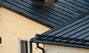 Detaljerad vy av en mörk plåttak konstruktion över ett gult hus med fönster.