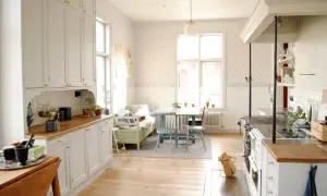 Ljust kök med vita skåp, träbänkskivor och en gammal vedspis. Ett bord med stolar och en bäddsoffa skapar en mysig matplats i detta charmiga gamla hus.