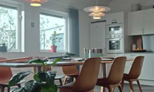 Ett ljust kontorsutrymme med köksdel. Bord med stolar, fönster med växter. Tänk på byggkostnad per kvadratmeter kontor vid inredning.