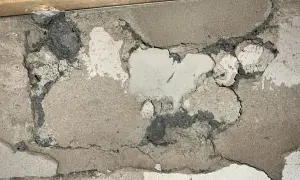 Skadad vägg med mörkgrå, smulig massa som kan vara blåbetong med asbest. Sprickor och avskalningar syns tydligt.