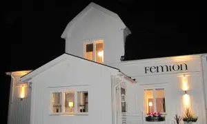 Vitt hus med svarta knutar, upplyst på kvällen. Namnet "Femton" syns ovanför ett fönster.
