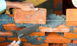 En murare lägger en ny tegelsten med en spackel. Arbetet är en del av att renovera tegelhus.