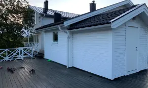 Vitt hus med mörk takläggning, en del av taket är under utbyggnad. Två sparkcyklar ligger på altanen.