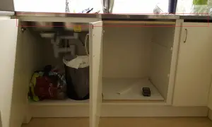 Under diskbänken pågår förberedelser för att installera diskmaskin i skåp. Syns rör, en papperskorg och diverse påsar.
