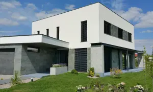 Modernt hus med vit, grå putsad fasad och stenbeklädda partier. Grönskande trädgård och garage.