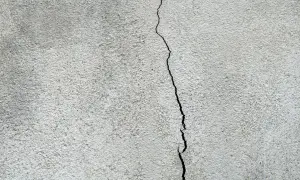 En spricka löper genom en grå, putsad fasad. Dags att laga sprickor i putsad fasad för att skydda huset.