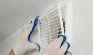 Händer med handskar rengör ett ventilationsgaller för att förbättra dammigt hemma ventilation.