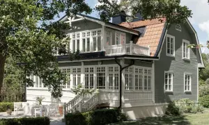 Ett charmigt grått hus med svarta knutar, omgivet av grönska. Ett vackert hus med många fönster och en veranda.