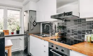Modernt kök med vit inredning, träbänkskiva och svart kakel. Kylskåp, diskho och spis. Perfekt för att laga god mat.
