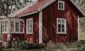 Rött torp med vit veranda och en cykel parkerad utanför. En idyllisk svensk sommaridyll.