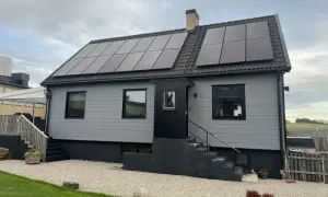 A light gray house with solar panels on the roof and a brick chimney.