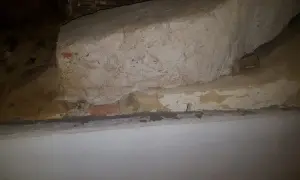 Detaljerad vy av en gammal murstock som är i behov av att riva murstock. Synliga tegelstenar och puts.