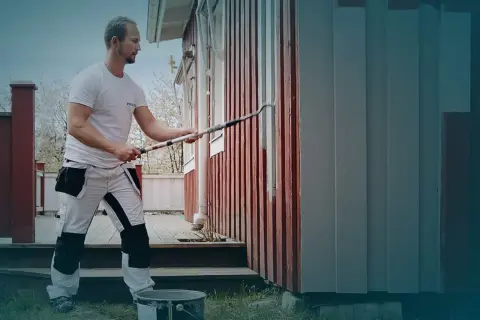 Ett tegelhus med en tillbyggnad i mörk träpanel under ett tegeltak. Uteplats med möbler och grönskande trädgård.
