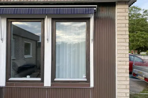 Två fönster med mörkbrun karm och en randig markis ovanför. En ny fasad utanpå den gamla, med träpanel och tegel.