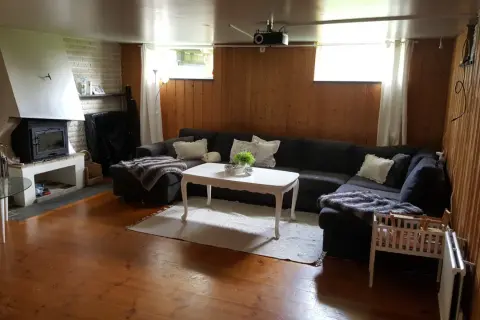 En mysig gillestuga med stor soffa, öppen spis och träpaneler. Perfekt för att renovera gillestuga till ett modernt allrum.