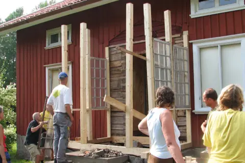 Byggnation av glasveranda entre. Människor hjälps åt att bygga en ny entré med gamla fönster.
