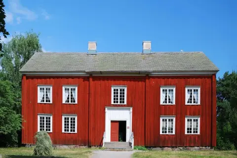 Rött trähus med vita fönster och skorstenar. En höstack ligger framför. Tänk på ventilation i gamla hus när du ser detta.