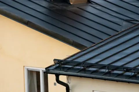 Detaljerad vy av en mörk plåttak konstruktion över ett gult hus med fönster.