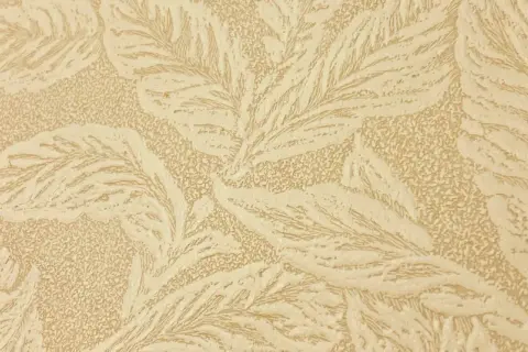 En beige tapet med ett mönster av stiliserade blad, typiskt för en tapet 1940-tal. Mönstret har en texturerad yta.