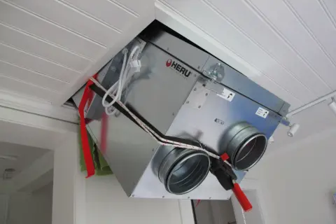 Ett FTX-aggregat vindmonterat i taket. Enheten är av märket HERU och har anslutningar för ventilation.