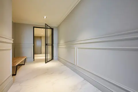 Elegant hall med stuckatur och marmorgolv. En öppen glasdörr leder in till ett ljust rum.