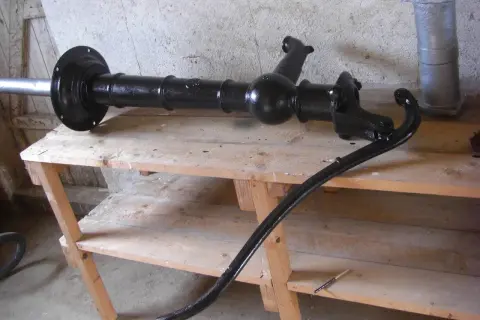 Svartmålad gårdspump, redo för renovering. Den ligger på en träbänk i ett garage.