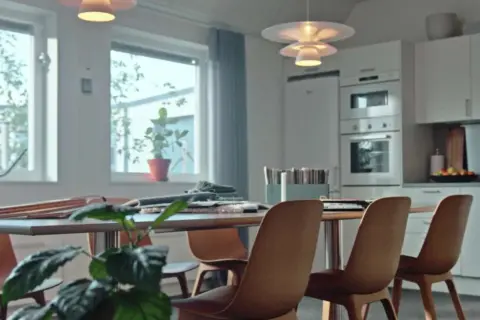 Ett ljust kontorsutrymme med köksdel. Bord med stolar, fönster med växter. Tänk på byggkostnad per kvadratmeter kontor vid inredning.