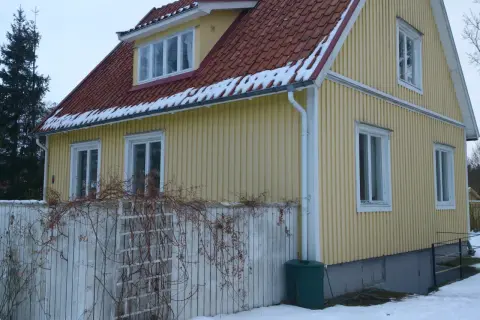 Gult 40-talshus med tegeltak och snö på takfoten. Ett staket med klätterväxter löper framför huset. Planer på att renovera 40-talshus?