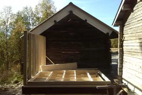 Bygga ut timmerhus. Ny stomme reses vid ett gammalt timrat hus.