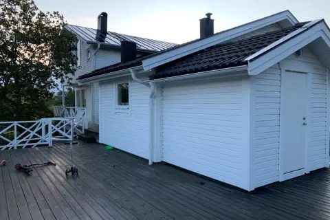 Vitt hus med mörk takläggning, en del av taket är under utbyggnad. Två sparkcyklar ligger på altanen.
