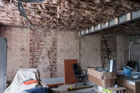 Bygga om hus: synliga bjälkar, isolering och tegelväggar vittnar om renovering. Material och verktyg ligger utspridda.