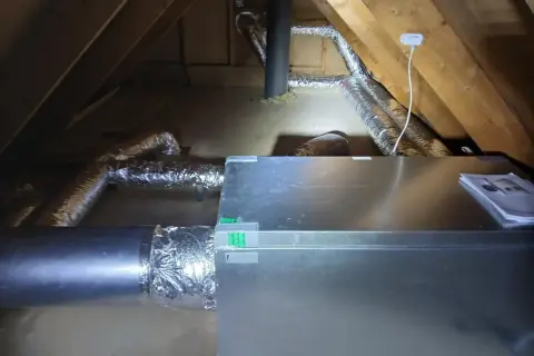Ventilationssystem i en vind med isolerade rör och en aggregatbox. Systemet är installerat för att hantera kallras och säkerställa god luftkvalitet.
