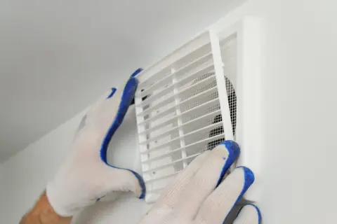 Händer med handskar rengör ett ventilationsgaller för att förbättra dammigt hemma ventilation.