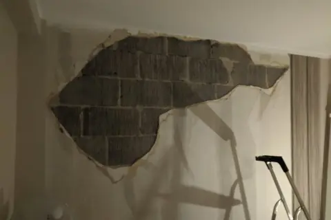 Stor fläck av puts som lossnat från en tegelvägg inomhus. En stege står redo för att laga puts inomhus.