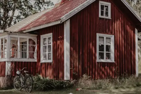 Rött torp med vit veranda och en cykel parkerad utanför. En idyllisk svensk sommaridyll.