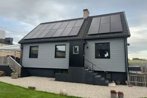 A light gray house with solar panels on the roof and a brick chimney.