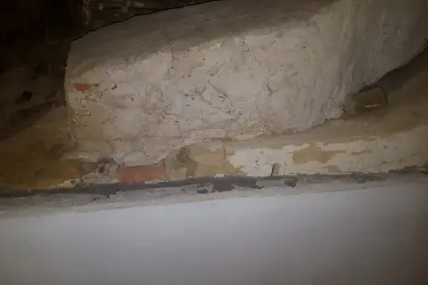 Detaljerad vy av en gammal murstock som är i behov av att riva murstock. Synliga tegelstenar och puts.