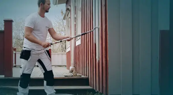 Ett tegelhus med en tillbyggnad i mörk träpanel under ett tegeltak. Uteplats med möbler och grönskande trädgård.