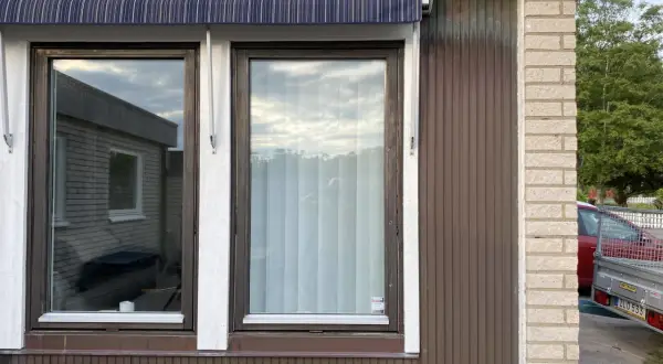 Två fönster med mörkbrun karm och en randig markis ovanför. En ny fasad utanpå den gamla, med träpanel och tegel.