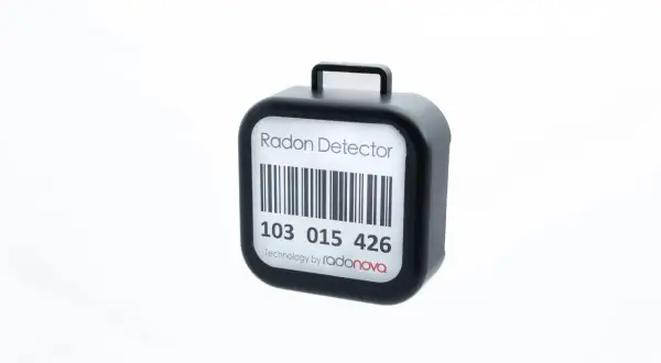 En svart radonmätare med streckkod och texten "Radon Detector". Kanske en present från grannar för att mäta inomhusluften.