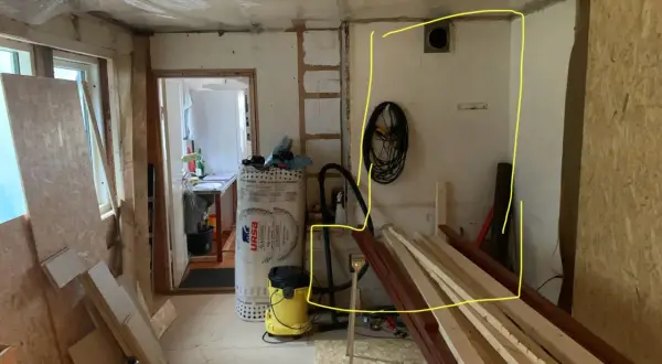 Renovering pågår. Gips mot murstock, isolering, byggmaterial och verktyg syns.
